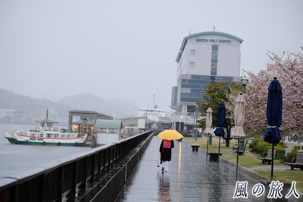 尾道　黄色い傘を刺した小学生と駅前桟橋の様子を写した写真